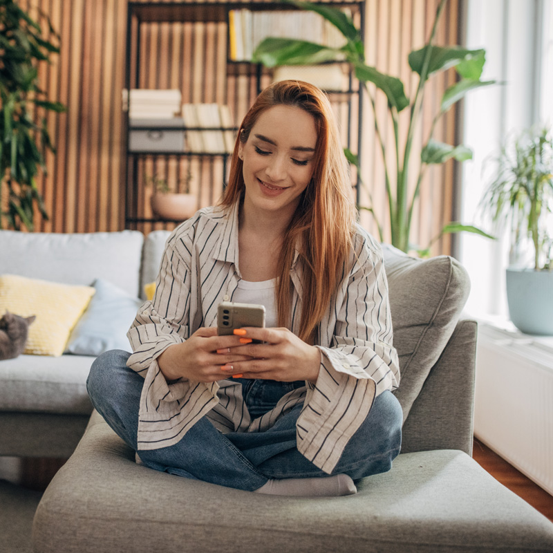 Woman sitting on a sofa and browsing teletherapy services in Houston, TX.